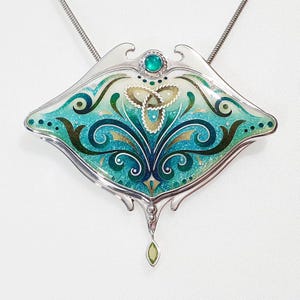 Op de afbeelding: Een zilveren ketting met een hanger met een groen en blauw emaille ontwerp. De hanger heeft een Keltisch knoop en een traanvormige hanger.