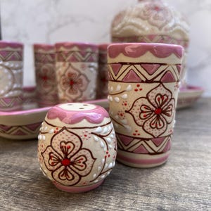 Puede incluir: Un juego de vajilla de cer&aacute;mica con un salero, un vaso alto y una botella. Las piezas est&aacute;n decoradas con un estampado floral en rosa y blanco, con detalles en marr&oacute;n. El juego incluye una bandeja y varios vasos.