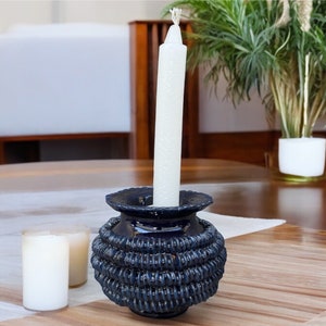 May include: A blue ceramic candle holder with a textured design holds a white candle. The candle holder is on a wooden table.