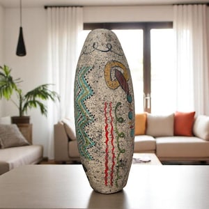 May include: A tall, oval-shaped decorative stone sculpture with colorful painted designs. The artwork features teal, yellow, red, and green patterns. The sculpture is placed on a gray table in a living room setting.