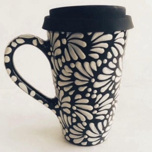 Puede incluir: Una taza de viaje de cer&aacute;mica negra y blanca con un patr&oacute;n floral. La taza tiene una tapa negra con un sello de silicona.