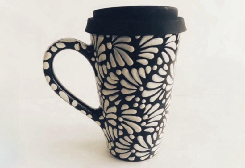 Puede incluir: Una taza de viaje de cer&aacute;mica negra y blanca con un patr&oacute;n floral. La taza tiene una tapa negra con un sello de silicona.