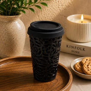 May include: A black ceramic travel mug with a raised, intricate floral relief pattern and a solid black silicone lid. The mug features a glossy finish that catches the light, highlighting the detailed texture of the embossed roses across the surface.