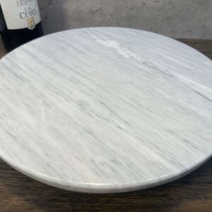 May include: White marble round serving tray with a smooth, polished surface. The tray has a natural veined pattern.