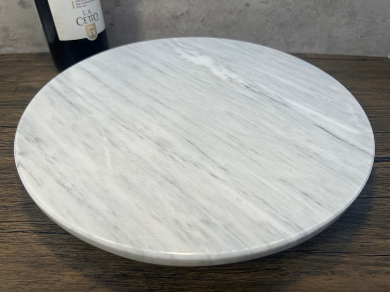 May include: White marble round serving tray with a smooth, polished surface. The tray has a natural veined pattern.