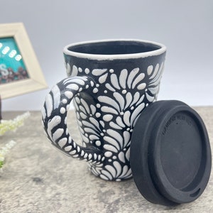 Puede incluir: Taza de cer&aacute;mica negra y blanca con un dise&ntilde;o floral y una tapa de silicona negra.
