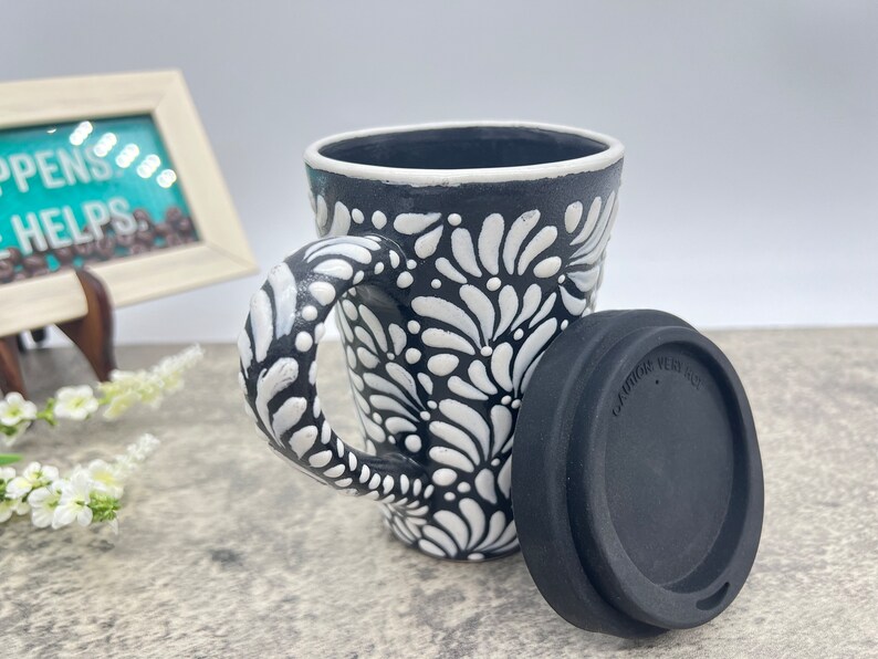 Puede incluir: Taza de cer&aacute;mica negra y blanca con un dise&ntilde;o floral y una tapa de silicona negra.