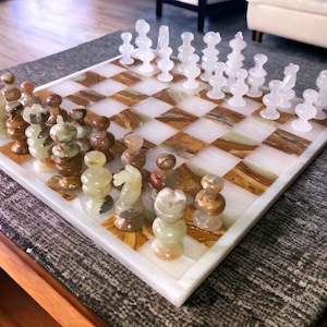 Peut inclure: Un jeu d'échecs en onyx blanc avec des pièces en marbre brun et vert sur un échiquier en onyx blanc. L'échiquier a un motif en damier brun et blanc.