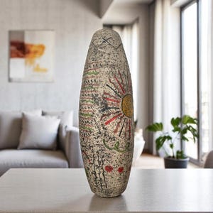 May include: A tall, textured vase with a hand-painted design. The vase features a central sunburst motif in yellow, red, and black, with additional patterns in green and red. The vase is approximately 24 inches tall.
