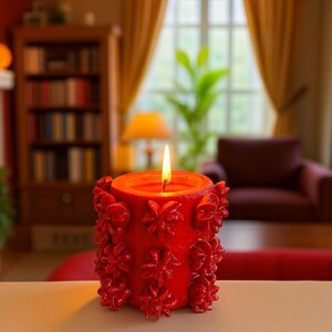May include: A lit, red candle with a floral design. The candle is cylindrical and has a textured surface with raised flower-shaped embellishments. The flame is bright against the red wax, suggesting a warm ambiance.