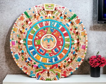 May include: A colorful, circular, decorative wall hanging with intricate carvings and designs. The center features a circular design with a face in the middle. The outer ring features a series of squares with different colors and designs.