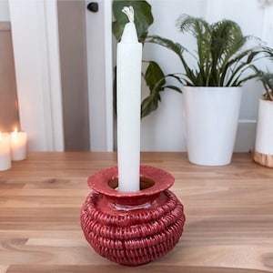 May include: A red ceramic candle holder with a white candle. The holder has a textured, woven design.