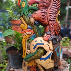 Peut inclure: Une sculpture en bois color&eacute;e d'un cr&acirc;ne avec un serpent et un aigle. Le cr&acirc;ne est peint dans des tons de brun, jaune et bleu. Le serpent est vert et jaune, et l'aigle est rouge et brun.