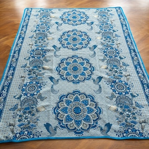 May include: A blue and white patterned throw blanket with a floral design. The blanket has a turquoise border and features a repeating pattern of stylized flowers and birds.
