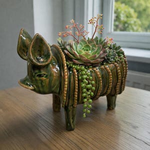 May include: A ceramic pig planter in shades of green and brown, filled with succulents and trailing plants. The planter has a detailed design with a glossy finish and is placed on a wooden table.