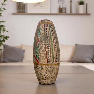 May include: A tall, decorative vase with a textured, off-white surface. The vase features vertical stripes in green, red, and black, with a gold band near the base. The design has an aged, rustic appearance, suitable for home decor.