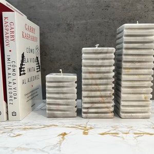 May include: Three white marble pillar candles with a textured surface. The candles are arranged in a row from largest to smallest.