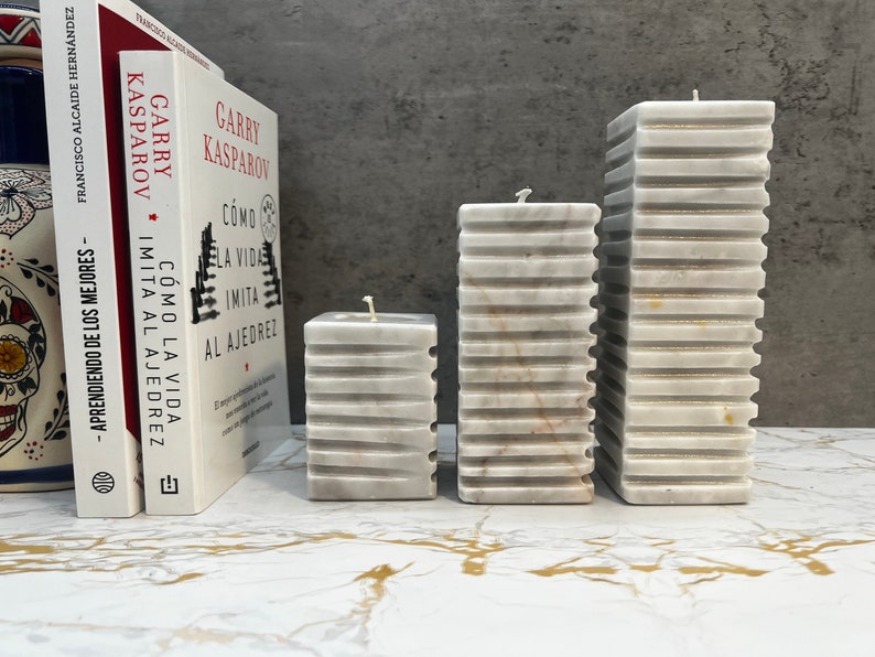 May include: Three white marble pillar candles with a textured surface. The candles are arranged in a row from largest to smallest.