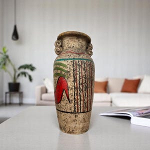 May include: A tall, beige ceramic vase with a textured surface and a wide opening. The vase features a red, green, and black painted design. It has two decorative handles on the sides. The vase is a decorative home decor item.