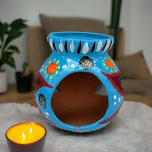 May include: A blue ceramic pot with a hole in the center. The pot is decorated with colorful geometric patterns and white dots.