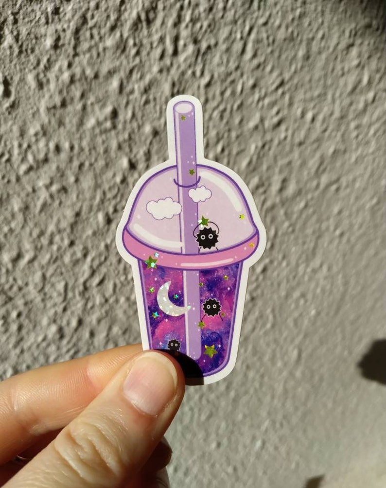 Puede incluir: Una pegatina con una taza de t&eacute; boba de dibujos animados con un dise&ntilde;o de galaxia. La taza es morada y rosa, con una pajita y una tapa. El contenido de la taza incluye una luna creciente, estrellas y peque&ntilde;as criaturas negras.