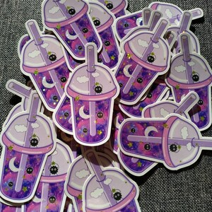 Puede incluir: Una colecci&oacute;n de pegatinas con un dise&ntilde;o de t&eacute; de burbujas morado y rosa. Las pegatinas tienen un fondo con tem&aacute;tica de galaxia con lunas, estrellas y un lindo personaje negro. Las tazas de t&eacute; de burbujas tienen tapa, pajita y acentos de nubes.