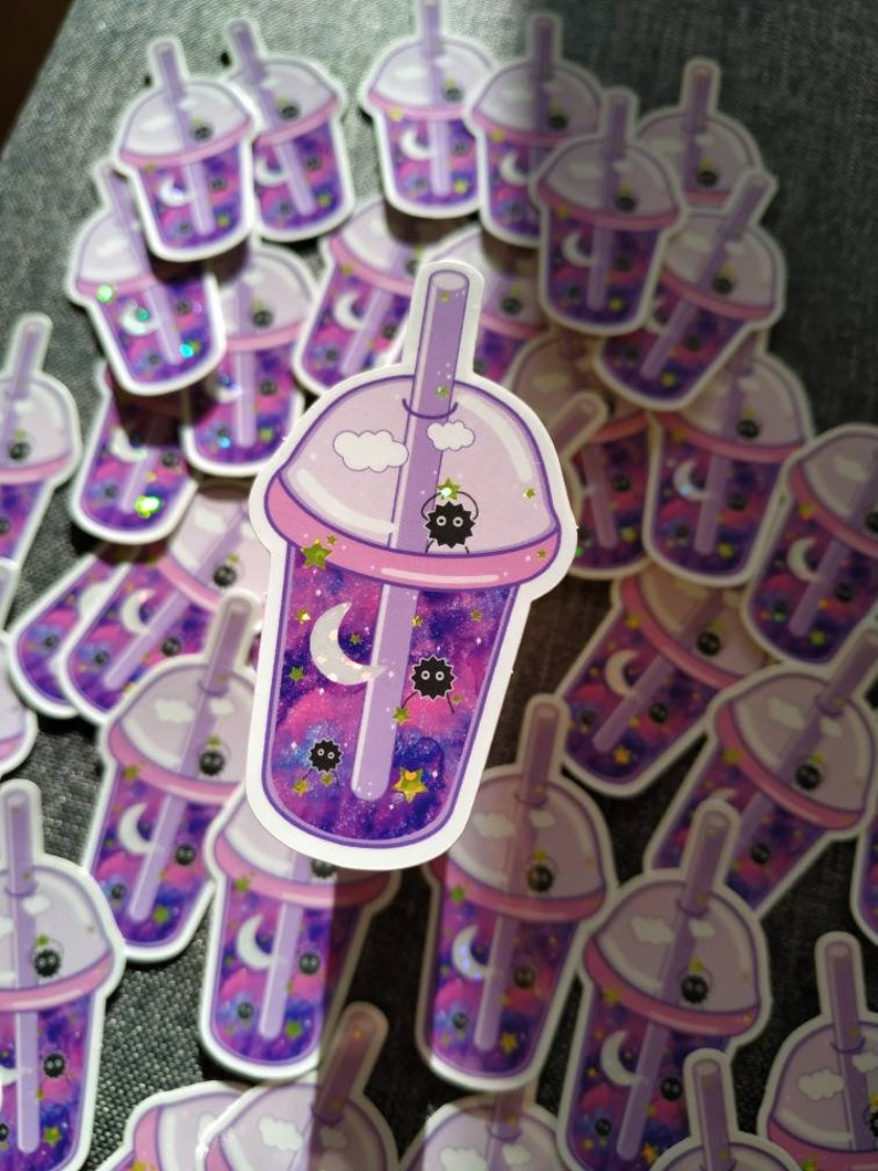 Puede incluir: Una colecci&oacute;n de pegatinas con un dise&ntilde;o de t&eacute; de burbujas morado. La taza de t&eacute; de burbujas tiene un interior con tem&aacute;tica de galaxia con una luna creciente, estrellas y un duende de holl&iacute;n negro. La taza est&aacute; rematada con una tapa y una pajita de color p&uacute;rpura claro.