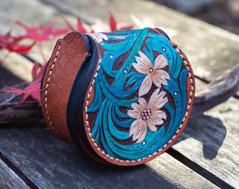 May include: A small, round, brown leather coin purse with a turquoise and white floral design. The purse has a black leather flap and a stitched edge.