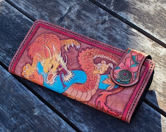 May include: A brown leather wallet with a detailed carving of a red and yellow dragon and floral accents. The wallet has a snap closure and a decorative metal button.