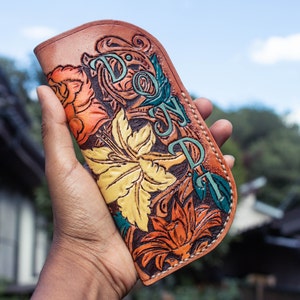 May include: A brown leather wallet with a floral design and the word "DON" in green lettering.