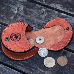 A brown leather coin purse with a flap opens and  there is two compartment for coins. hand stitched  and a small metal button closure.