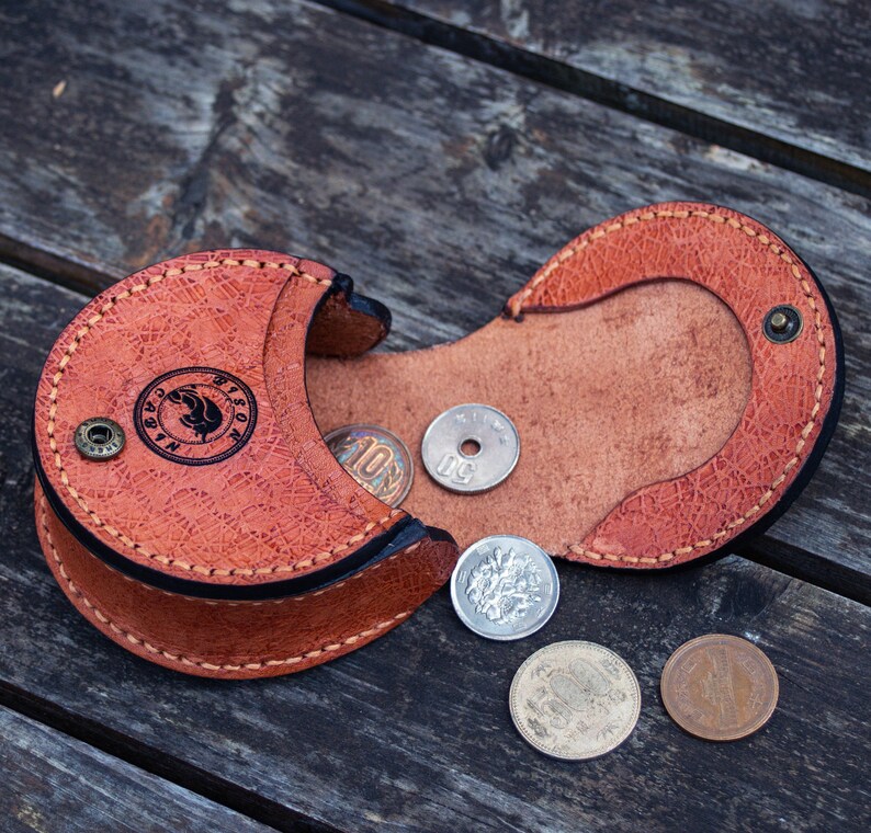 A brown leather coin purse with a flap opens and  there is two compartment for coins. hand stitched  and a small metal button closure.