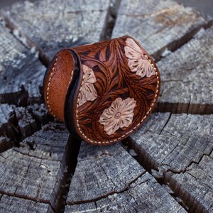 A brown leather coin purse with a floral design. The purse is decorated with light brown flowers  . The purse is flap open and button closer .