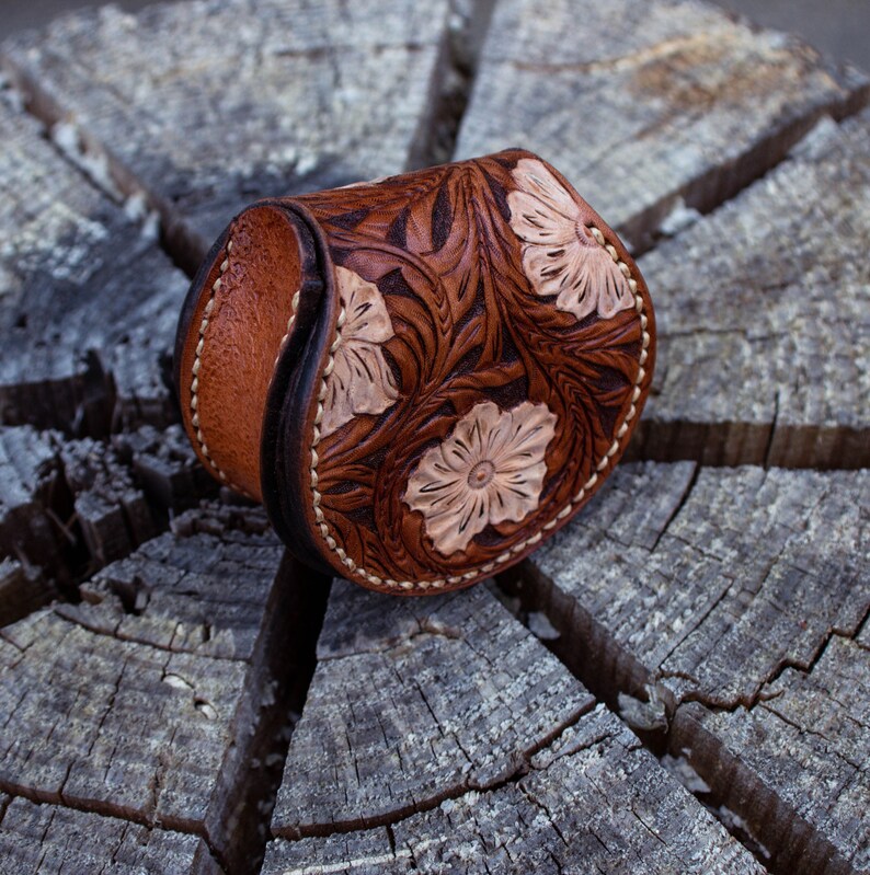 A brown leather coin purse with a floral design. The purse is decorated with light brown flowers  . The purse is flap open and button closer .