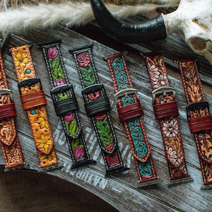 Könnte beinhalten: Eine Auswahl an Leder-Armbändern mit aufwendigen Blumen- und keltischen Knotenmustern. Die Armbänder in Braun-, Orange-, Grün- und Rottönen werden auf einer rustikalen Holzoberfläche präsentiert.