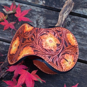 A leather coin wallet with a floral design. The wallet is brown with orange flowers and yellow color . The wallet is button closed and hand stitching