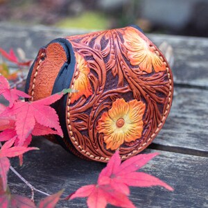 A small, round, brown leather coin purse with a floral design. This coin purse is hand tooled with western floral design