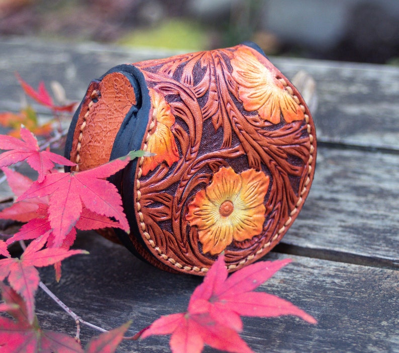 A small, round, brown leather coin purse with a floral design. This coin purse is hand tooled with western floral design