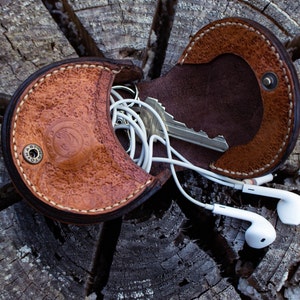 A brown leather coin,  key and headphone holder . hand stitched . Flap open and two compartments . button closer