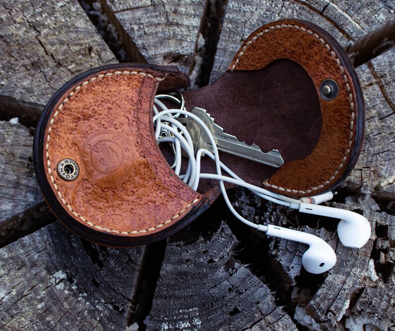 A brown leather coin,  key and headphone holder . hand stitched . Flap open and two compartments . button closer