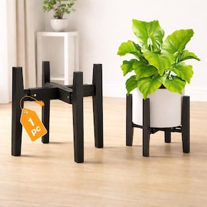 May include: Black wooden plant stand with a white ceramic pot holding a green leafy plant. The stand is adjustable and has a modern design. A second stand is shown without a plant. The tag says "1 pc".