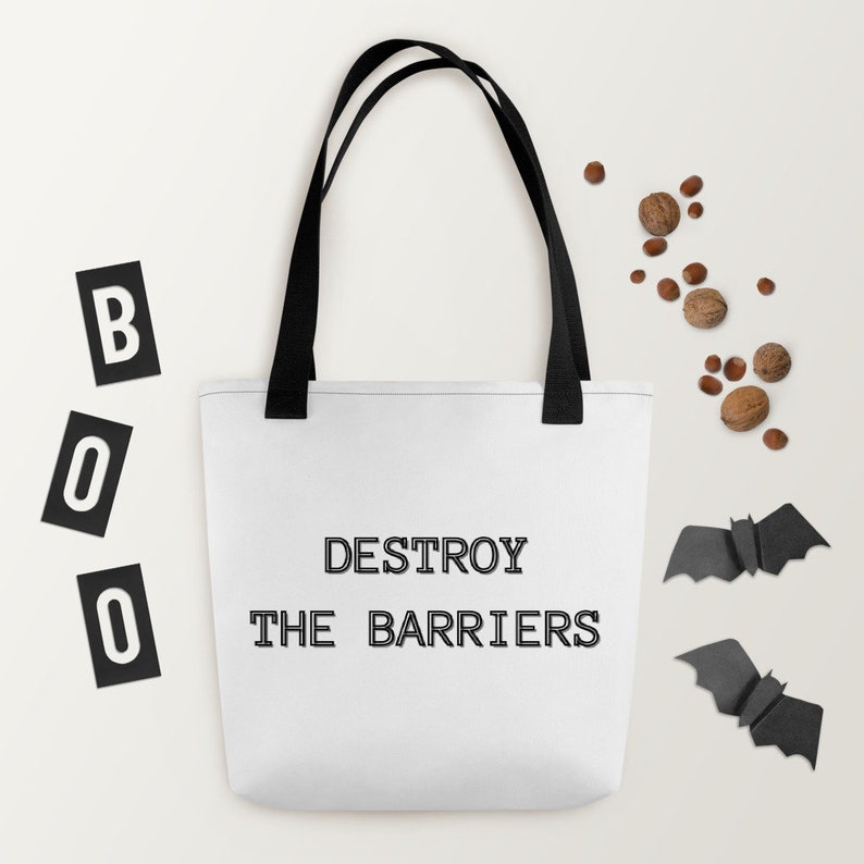 K&ouml;nnte beinhalten: Wei&szlig;e Einkaufstasche mit schwarzen Henkeln und dem Text "DESTROY THE BARRIERS" in Schwarz gedruckt. Die Tasche befindet sich auf einem wei&szlig;en Hintergrund mit schwarzen Buchstaben, die "BOO" buchstabieren, und zwei schwarzen Papierflederm&auml;usen.