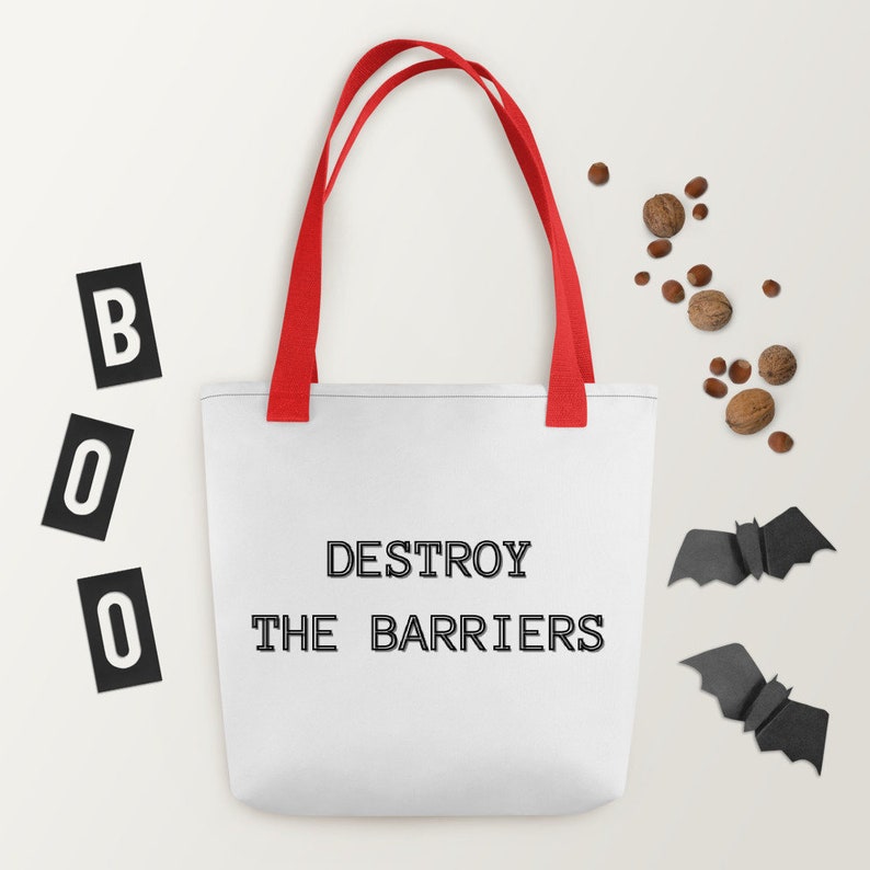 K&ouml;nnte beinhalten: Wei&szlig;e Einkaufstasche mit roten Henkeln und dem Text "DESTROY THE BARRIERS" in Schwarz gedruckt. Zwei schwarze Papierflederm&auml;use befinden sich auf beiden Seiten der Tasche.