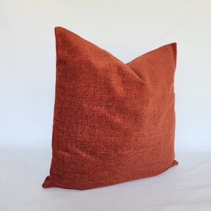 May include: A rust-colored throw pillow with a soft, textured fabric.