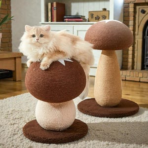 以下が含まれることがあります： ふわふわとした明るい色の猫が、キノコ型のキャットツリーの上にいます。キャットツリーは、茶色のサイザル麻の球がベージュの球の上にあり、茶色のベースが付いています。2つ目のキノコ型のキャットツリーが背景にあります。