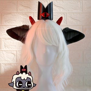 May include: A white wig with black and red devil horns and a black crown with a red eye on top. A cartoon image of a black and white sheep with a red eye and a red bell is in the bottom left corner of the image.