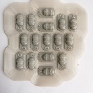 May include: A sheet of clear plastic with 18 gray, 3D printed, miniature barrels. The barrels have a decorative design and a small ring on the top.
