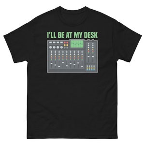 以下が含まれることがあります： 黒のTシャツに、緑色の「I'll be at my desk」という文字と、さまざまなノブやボタンが付いたサウンドボードのグラフィックがプリントされています。