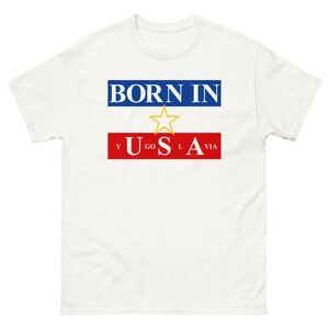 May include: White t-shirt with the text "BORN IN" in blue letters above a red bar with the text "Y GO L VIA" and a yellow star in the center. The text "USA" is in white letters on the red bar.
