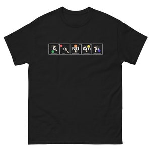 May include: Black t-shirt with a periodic table-style design spelling out "K-e-Nd-Am-Ta". Each element square features a colorful illustration and the element's name. The shirt is made of a soft, comfortable material.